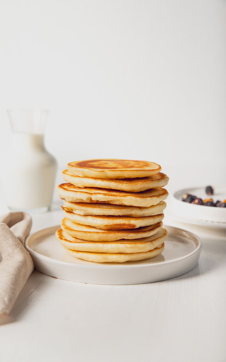 a stack of pancakes sitting on top of a white plate next to a glass of milk