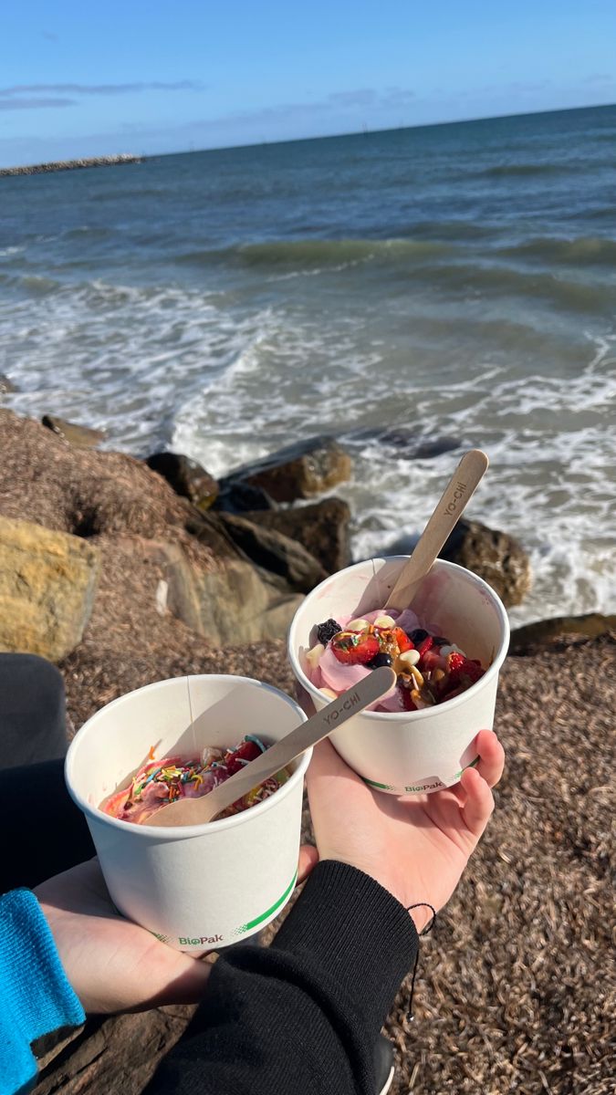 two people are eating ice cream at the beach with chopsticks in their hands