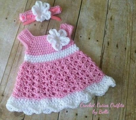 a pink and white crocheted dress laying on top of a wooden floor next to scissors