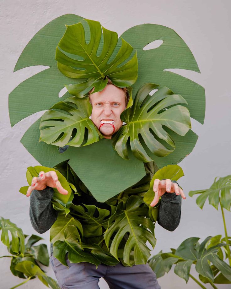 a man is wearing a fake monster's head surrounded by green leaves