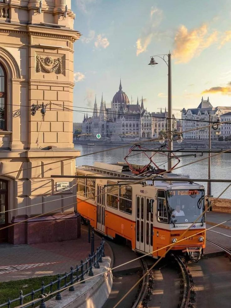 an orange trolley car traveling down the tracks next to a large body of water with buildings in the background