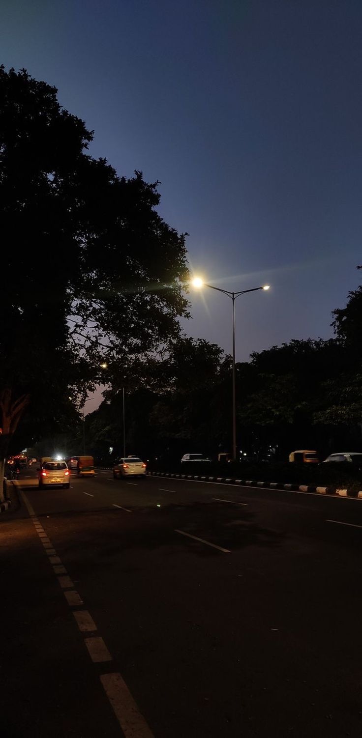 an empty street at night with cars parked on the side and trees in the background