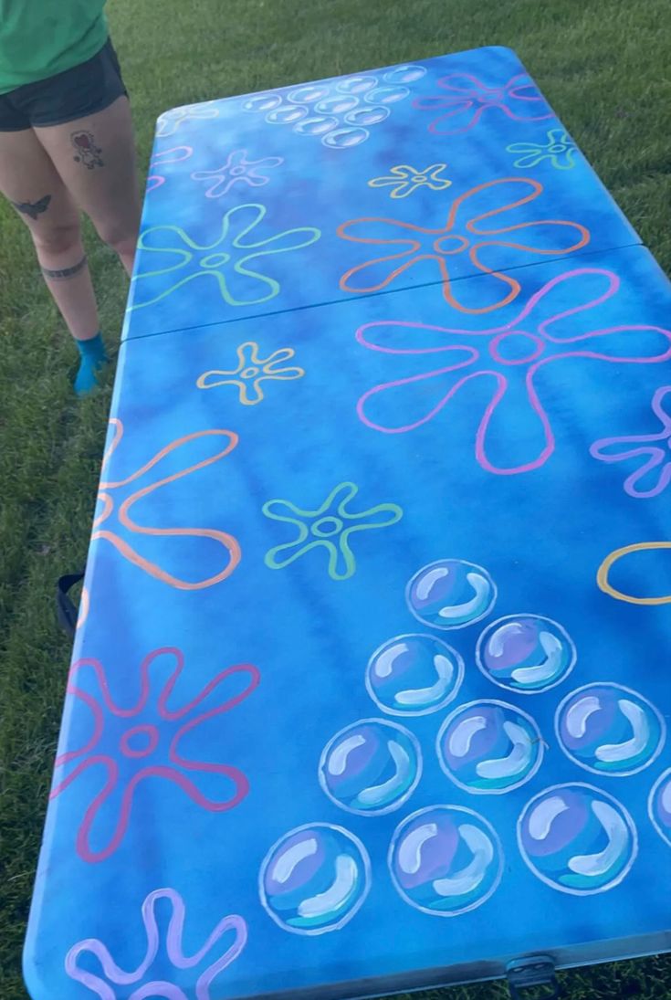 a woman standing next to a large blue board covered in colored circles and flowers on it