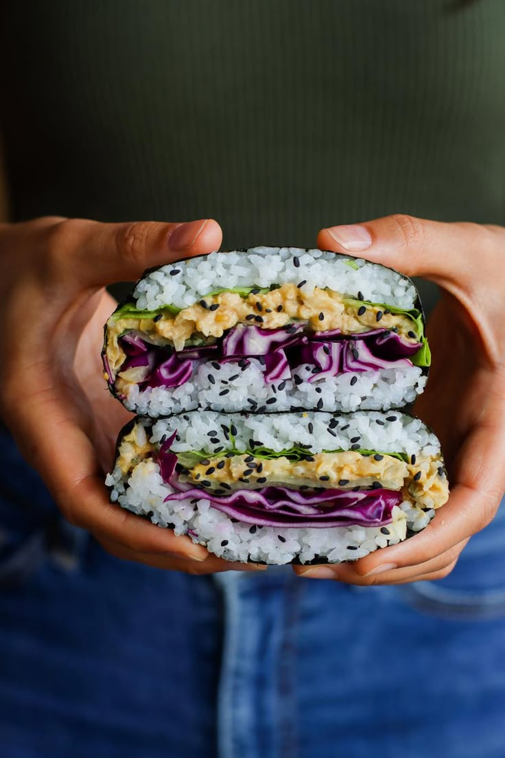 a person holding two sushi sandwiches with purple cabbage and cucumber on them