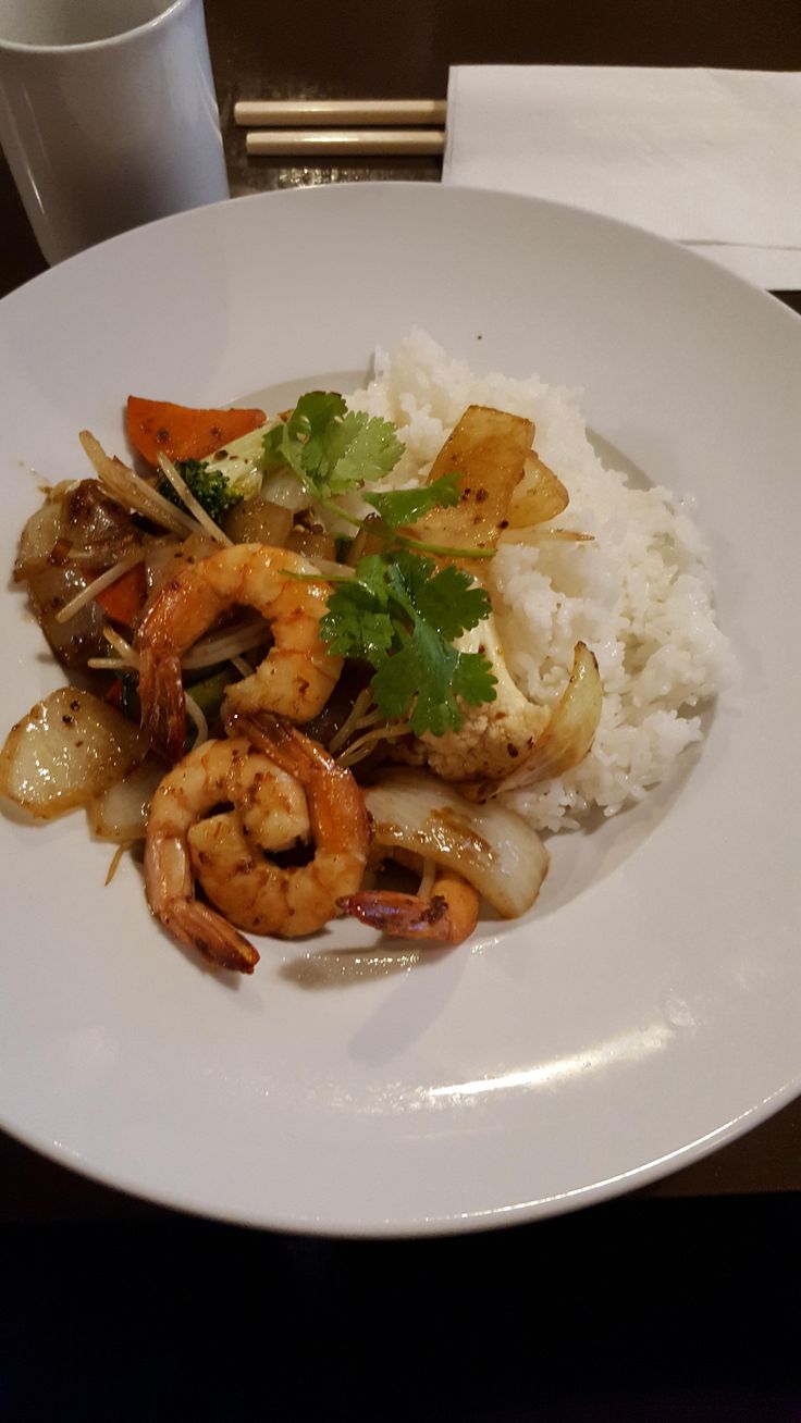 a white plate topped with shrimp, rice and veggies next to a cup