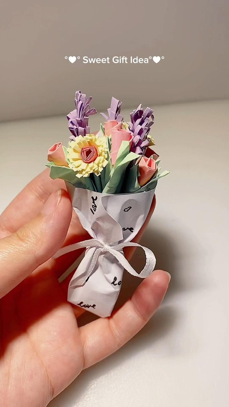 a hand holding a bouquet of flowers on top of a white table with the words sweet gift idea written above it