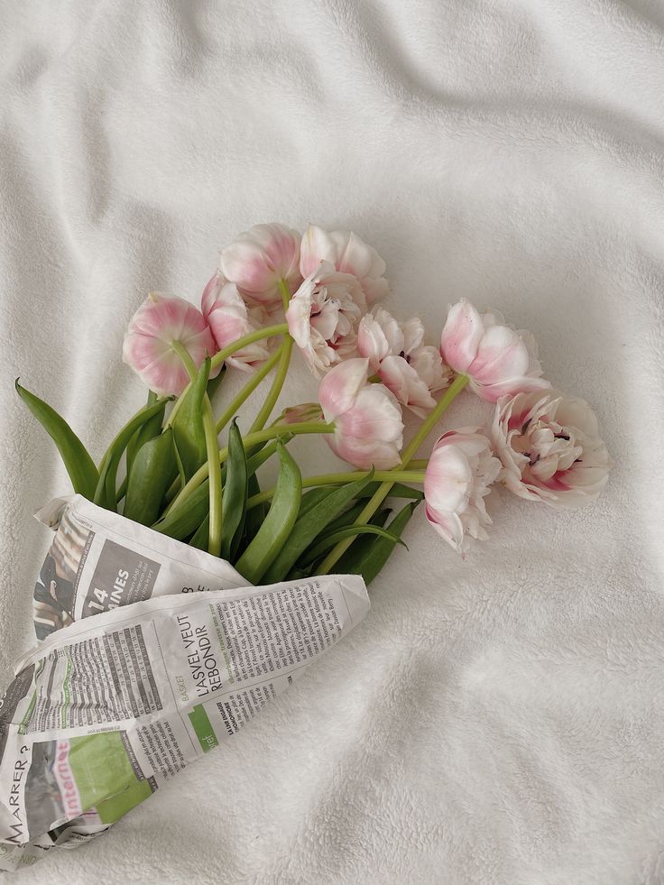 pink tulips are laying on a white sheet next to a news paper and newspaper