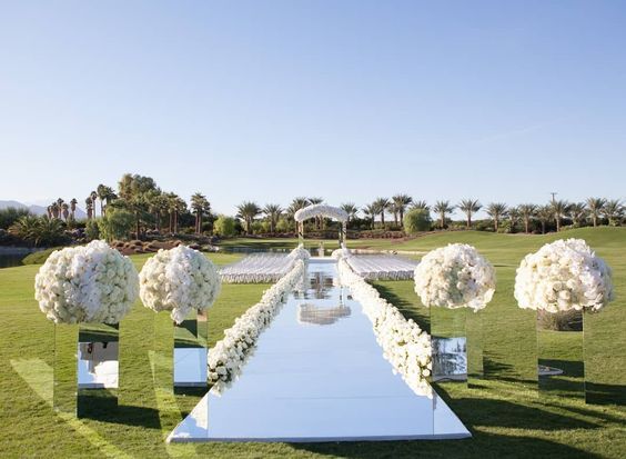 an outdoor ceremony setup with white flowers and greenery on the grass, in front of palm trees