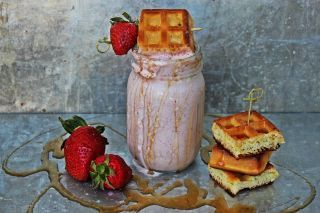 some strawberries are sitting on a plate next to a jar of milk and waffles