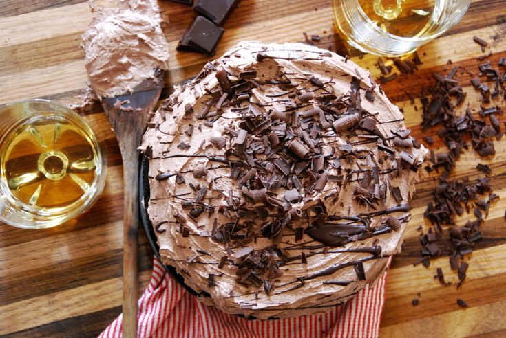 a cake with chocolate frosting sitting on top of a wooden table next to two glasses