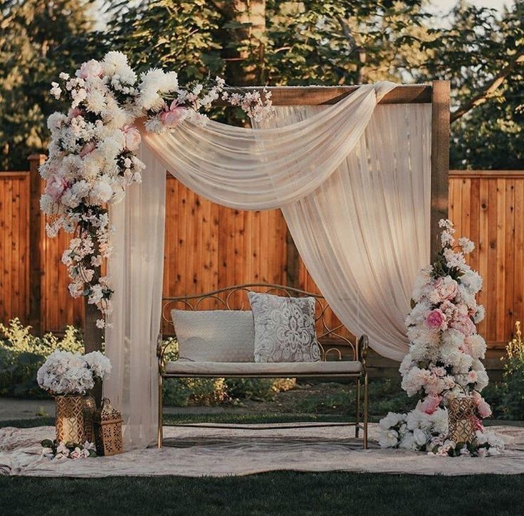 an outdoor wedding ceremony setup with flowers on the arch and white drapes draped over it