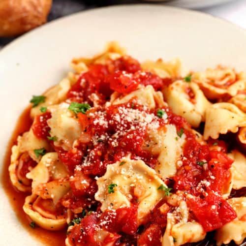 a white plate topped with pasta covered in marinara sauce and parmesan cheese