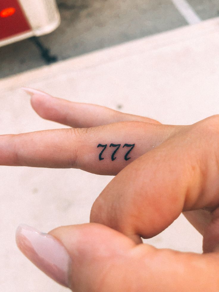 a person's hand with a small tattoo on the middle finger that reads 377