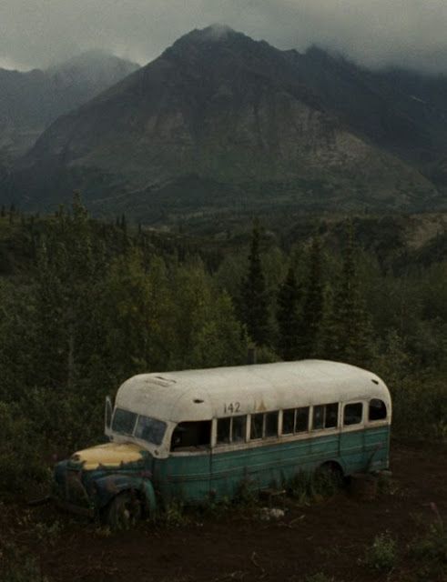 an old bus is sitting in the middle of a field with mountains in the background