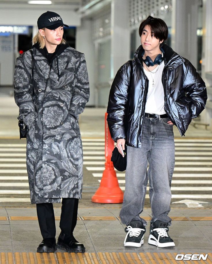 a man and woman standing next to each other in an airport terminal, both wearing coats