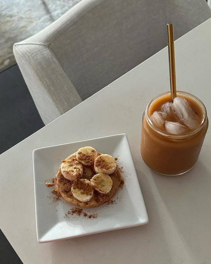 a white plate topped with banana slices next to a cup of iced coffee on top of a table