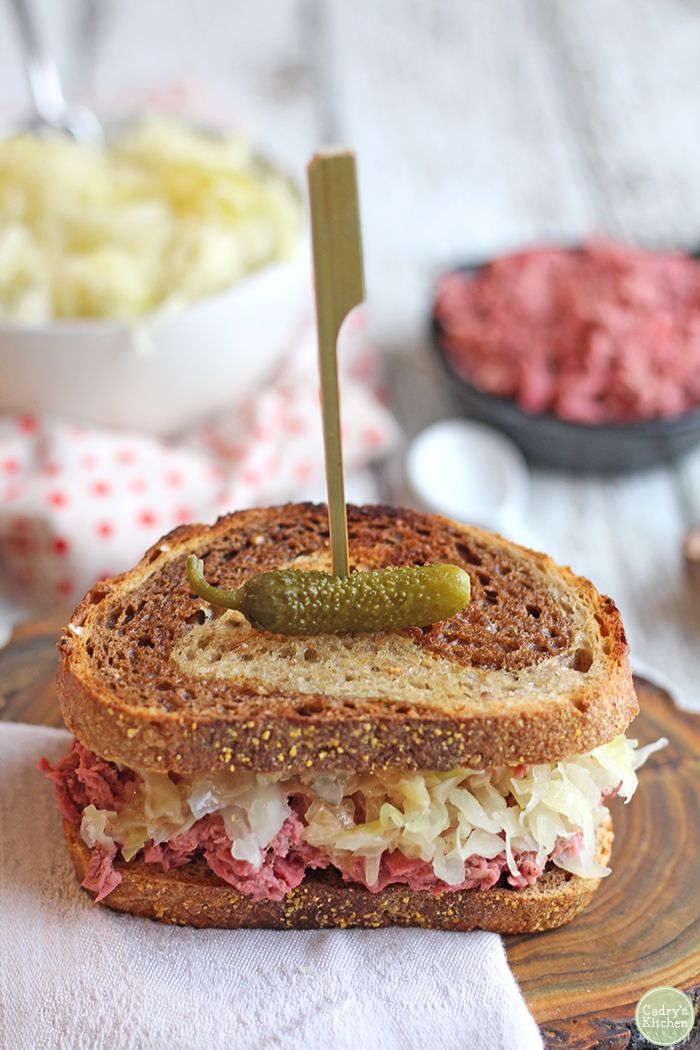 a sandwich on a plate with a pickle sticking out of the middle and other food in bowls behind it