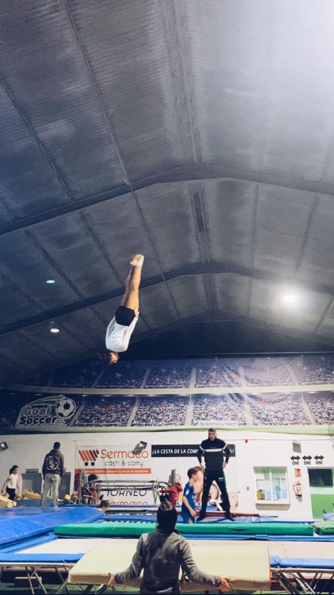 a man on a trampoline doing a trick in the air with other people watching