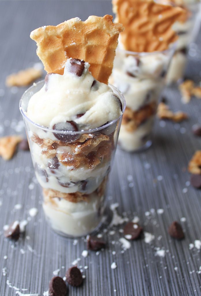 two cups filled with ice cream and waffles on top of a table covered in chocolate chips