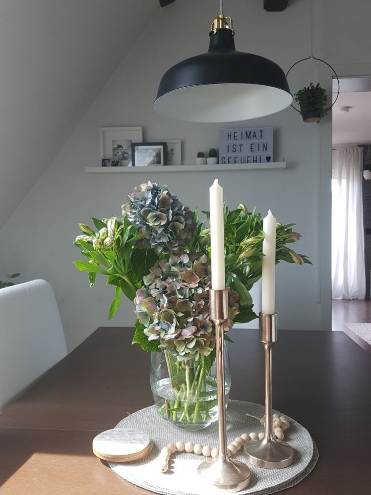 a vase with flowers and candles on a table in a room that has white walls