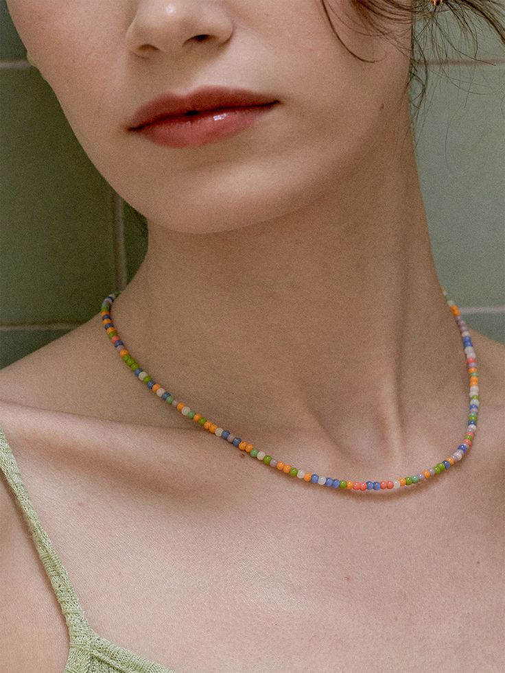 a woman wearing a necklace with multi colored beads on it's neck, standing in front of a green tile wall