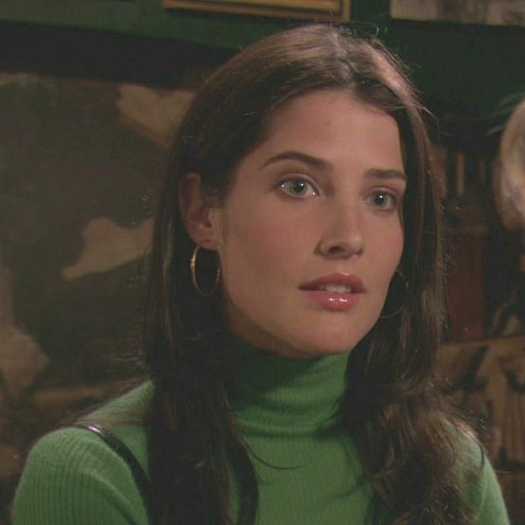 a woman with long hair wearing a green turtle neck sweater and earrings looking at the camera