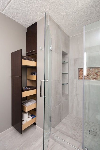 a walk in shower sitting next to a white tiled wall and wooden shelves on the side