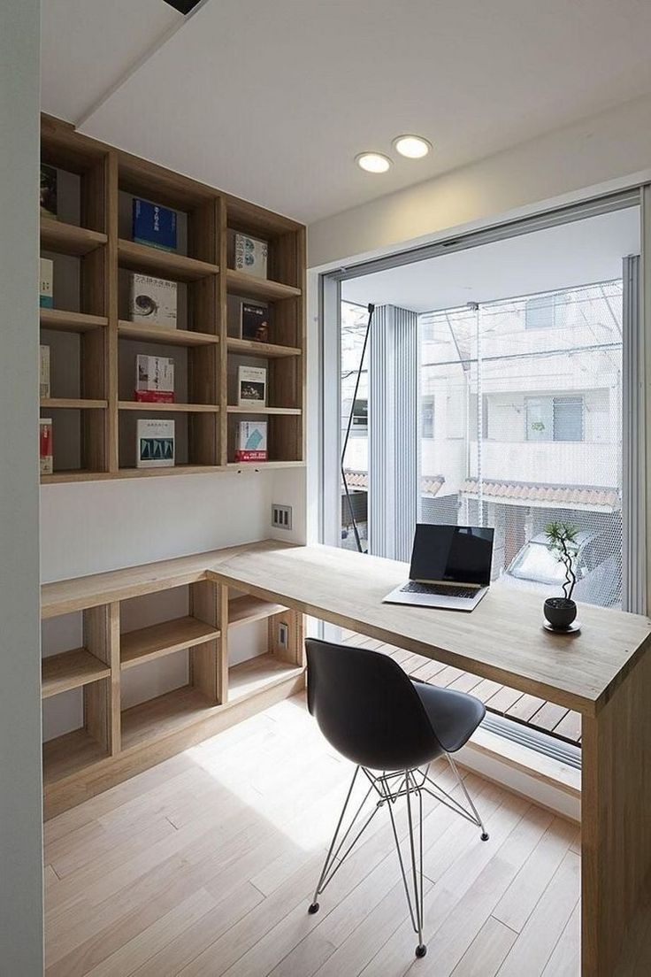 a desk with a laptop on top of it in front of a book shelf and window