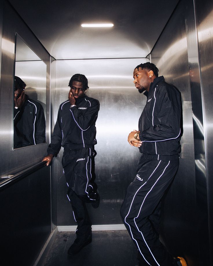 two men in black tracksuits standing on an elevator