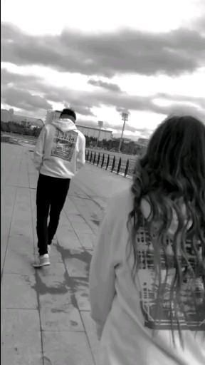 two people are walking down the sidewalk with their backs to each other, one is wearing a t - shirt and the other has long hair