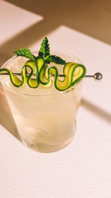 a drink with cucumber and mint garnish sitting on a white table