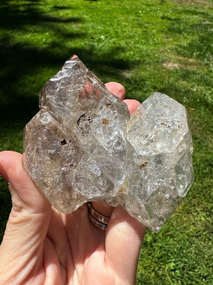 two pieces of clear rock sitting in the palm of someone's hand on green grass