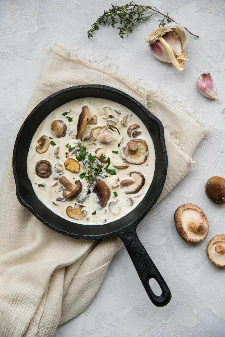 a skillet filled with mushroom soup on top of a white cloth next to mushrooms