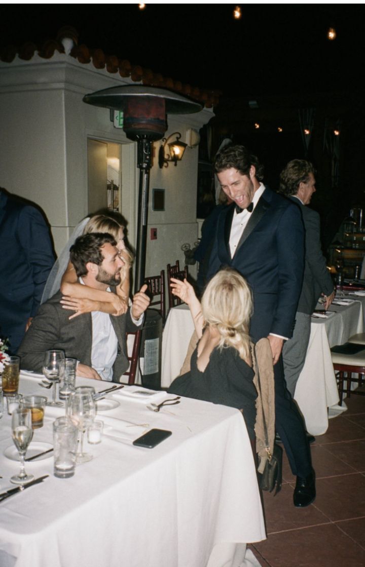 a group of people sitting around a table at a formal event with one man in a suit and the other woman in a white dress