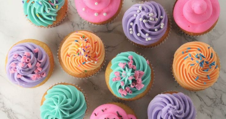 cupcakes decorated with colorful frosting and beach themed icing are displayed in a box