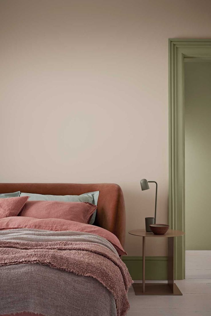 a bed sitting next to a green door in a room with pink sheets and pillows