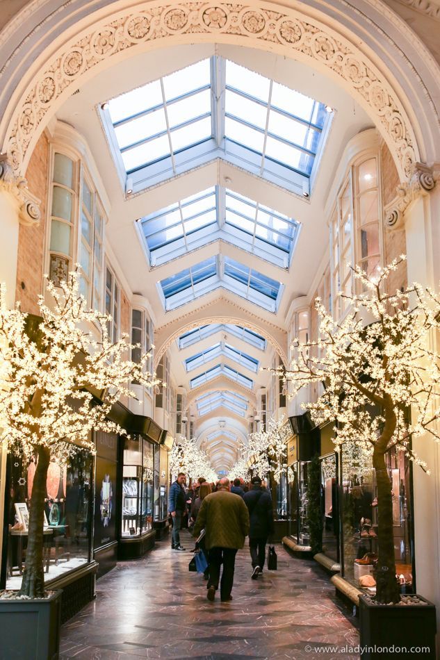 people are walking through an indoor mall with lights on the ceiling and windows above them