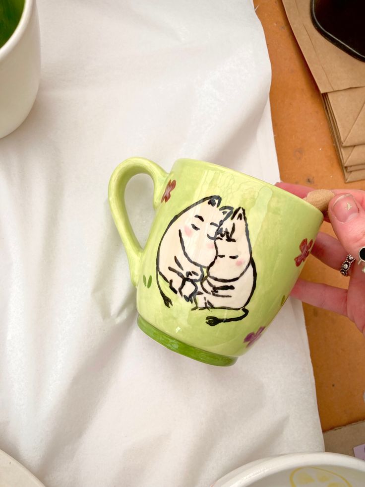 a person is holding a mug with a drawing on it and the cup has a spoon in it