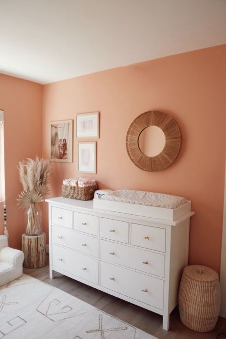 a baby's room with peach walls and white furniture