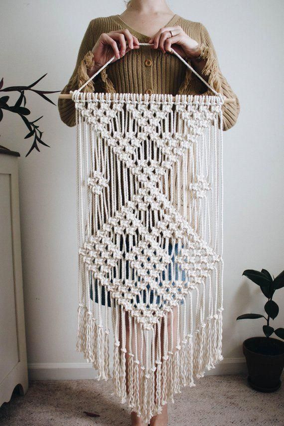 a woman holding up a white crocheted wall hanging