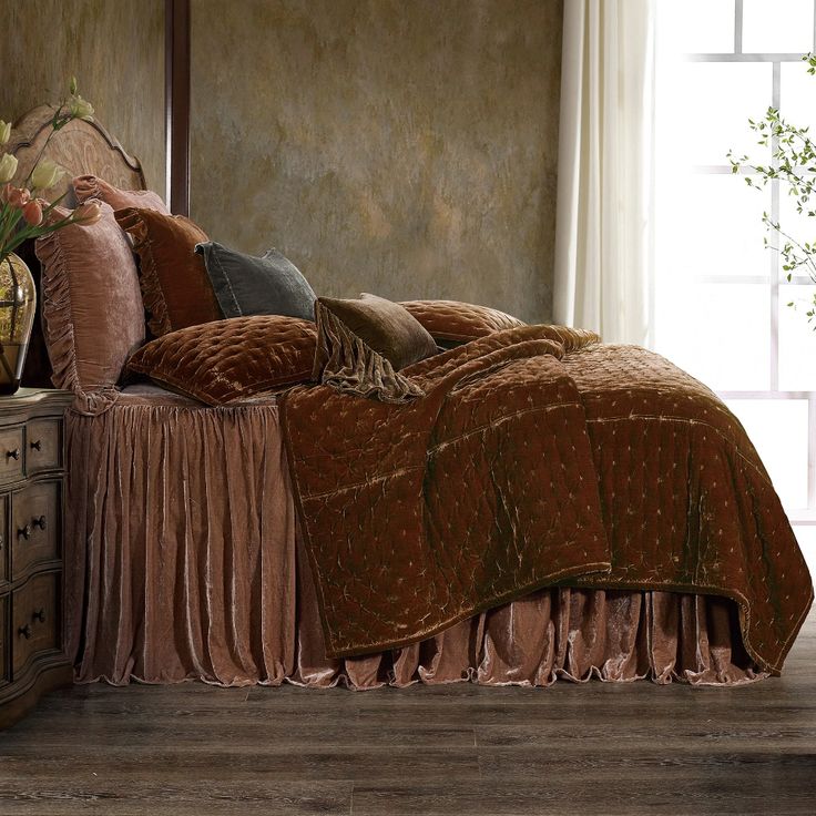 a bed with a brown bedspread and pillows on top of it next to a window