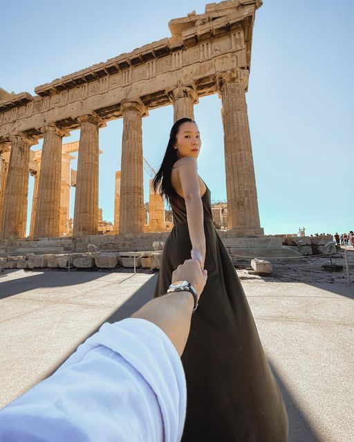 a woman holding the hand of another person in front of an ancient building with columns