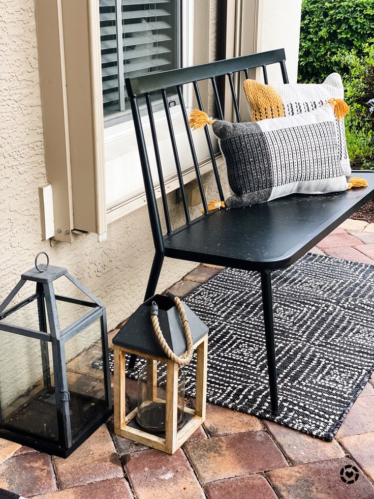 a black bench sitting on top of a brick patio next to a lamp and window