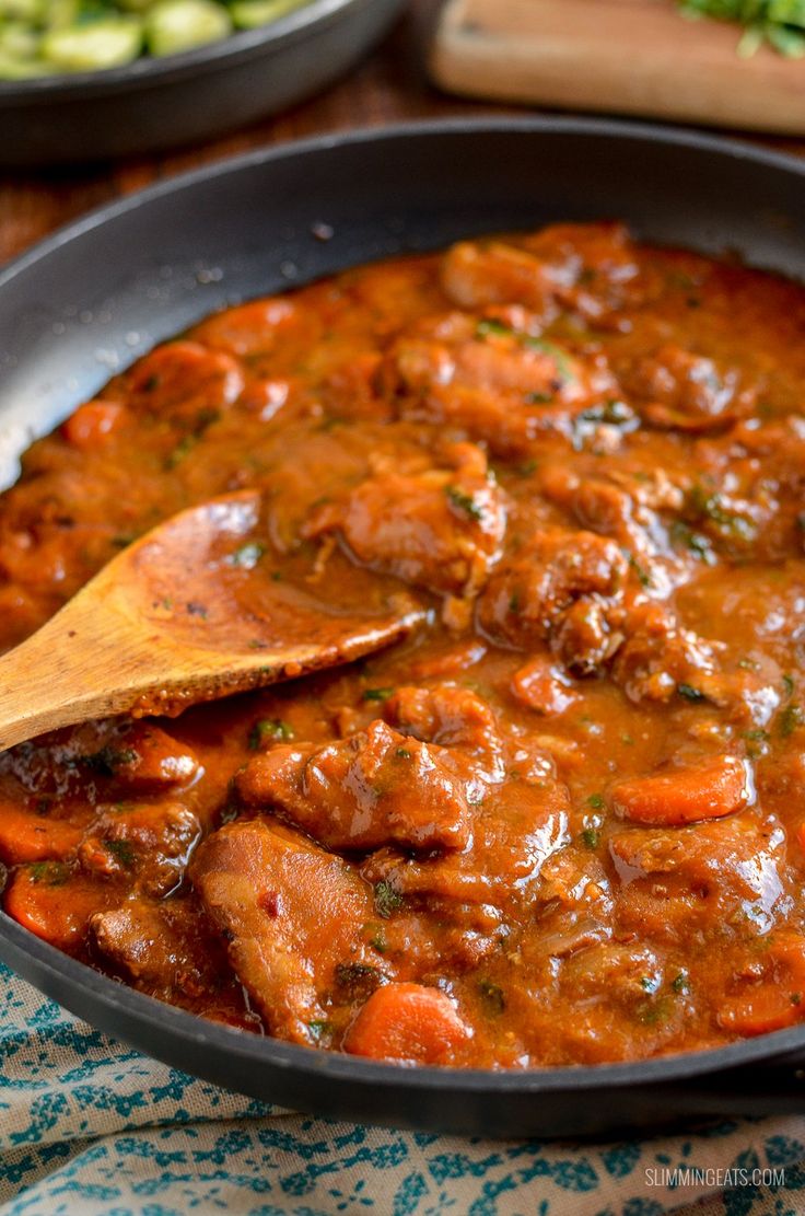 a skillet filled with meat and carrots on top of a table next to other food