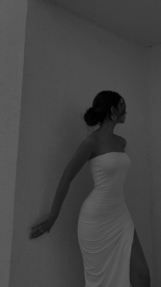 a woman in a white dress leaning against a wall