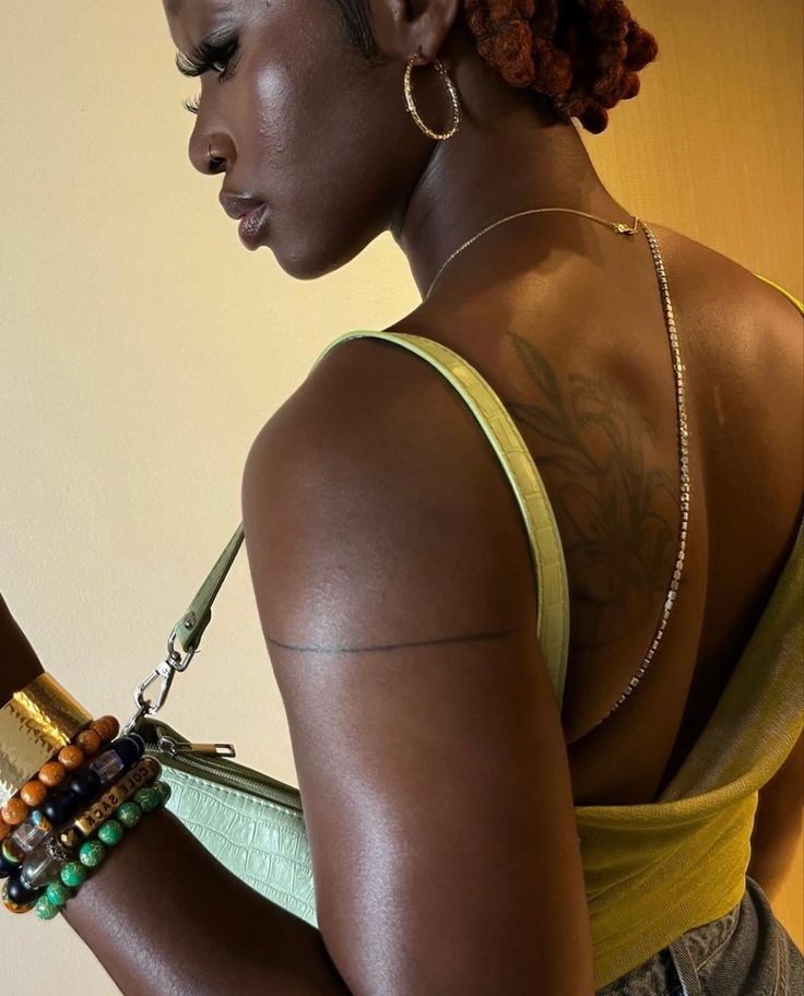 a woman with tattoos on her back holding a cell phone in her right hand and wearing bracelets around her neck