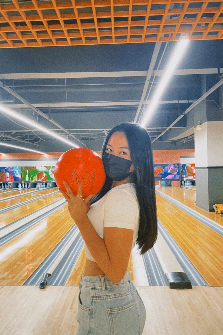 a woman wearing a face mask holding an orange frisbee in a bowling alley