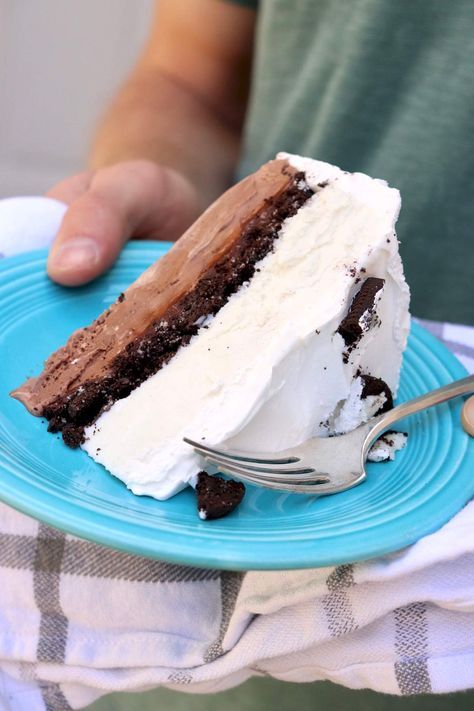 a person holding a plate with a piece of cake on it and a fork next to it