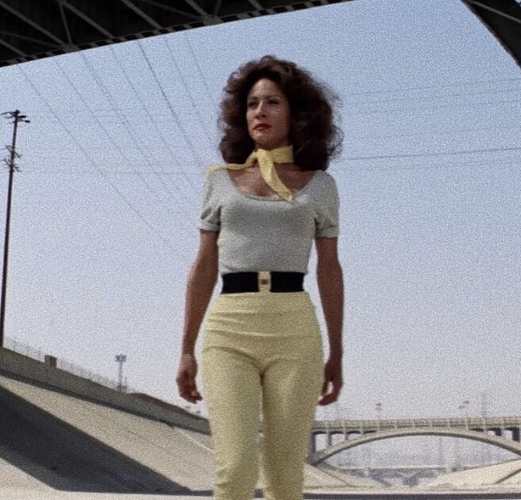 a woman is walking down the street with her skateboard in front of her and an overpass behind her