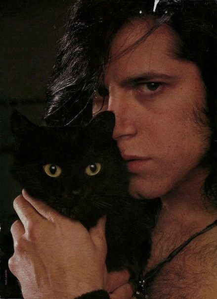 a man with long hair holding a black cat